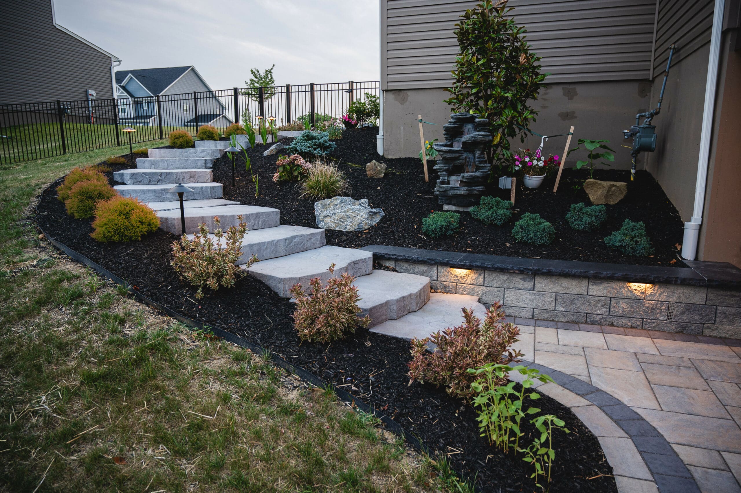 Modern stone-step garden lit at dusk with uplighting and fountain feature